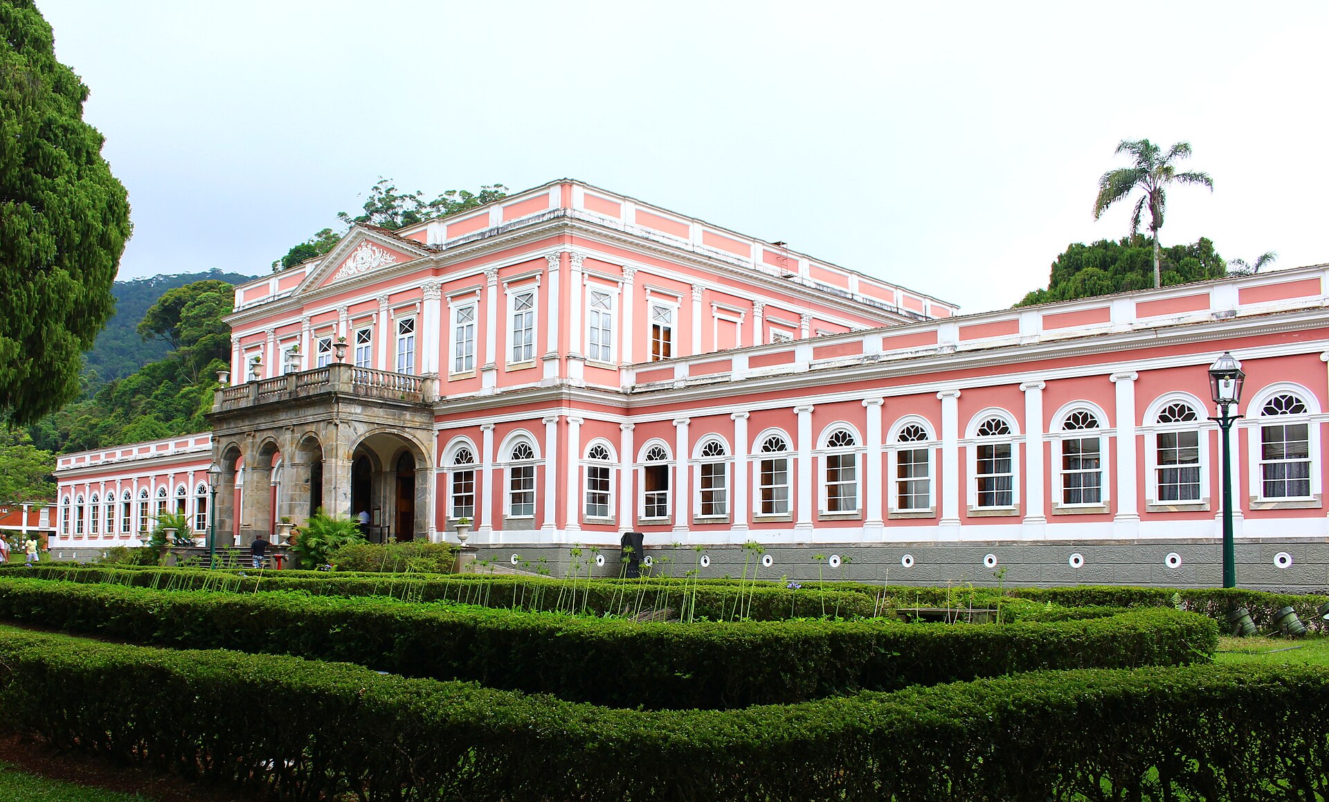 Fachada rosa do Museu Imperial de Petrópolis, jardim geométrico e morro ao fundo.